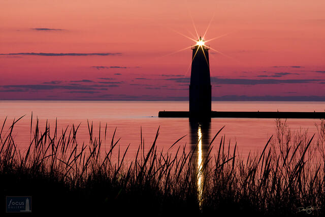Silhouette of the Frankfort Lighthouse and beach grass at sunset on Lake Michigan.