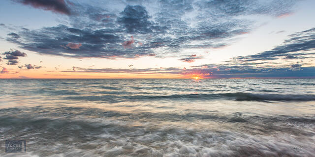 Panoramic sunset over Lake Michigan with blue water and skies and orange sun.