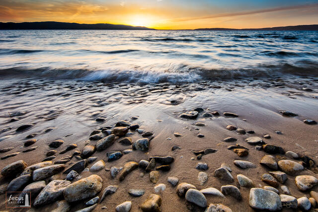 Photograph of waves at sunset on a rocky Crystal Lake shoreline in Benzie County, Michigan.