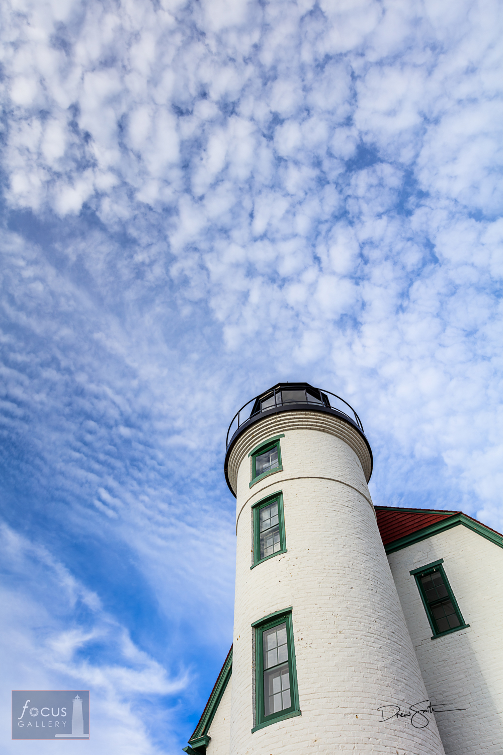 The   tower of the Point Betsie lighthouse climbs into a blue sky dotted with   clouds.