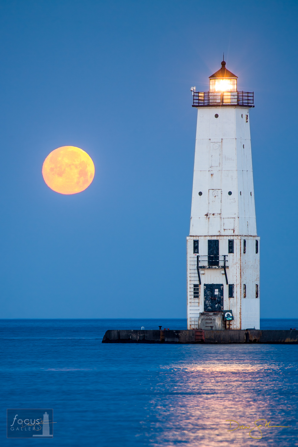 The full   moon sets into Lake Michigan over the Frankfort Lighthouse at dawn.