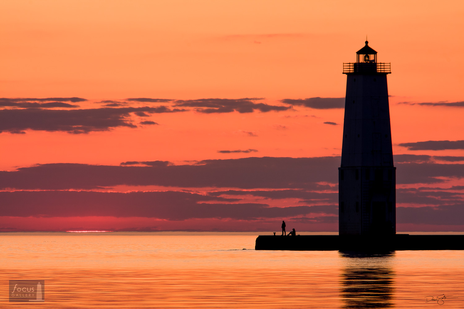 Sunset over Lake Michigan as two visitors watch from the Frankfort Lighthouse.