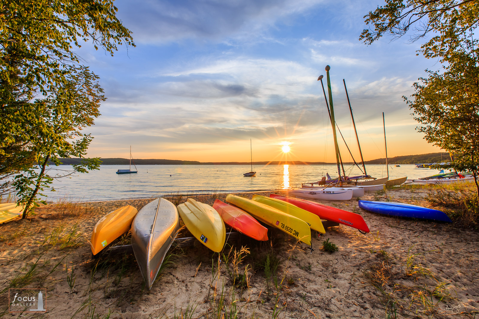 Sunset over Crystal Lake beach with canoes, kayaks and sailboats on the beach.