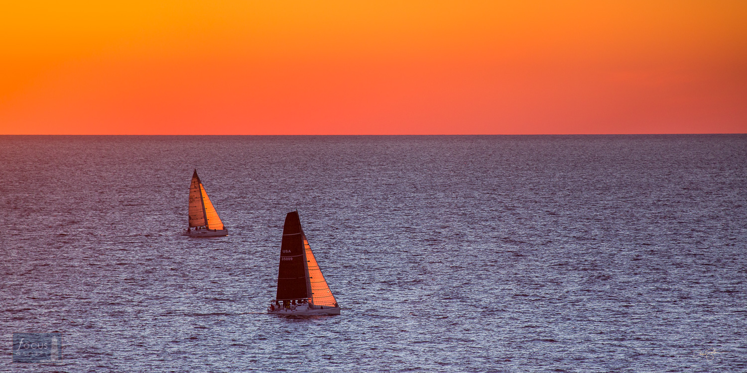 Two sailboats on Lake Michigan with sunset glow in the sky.