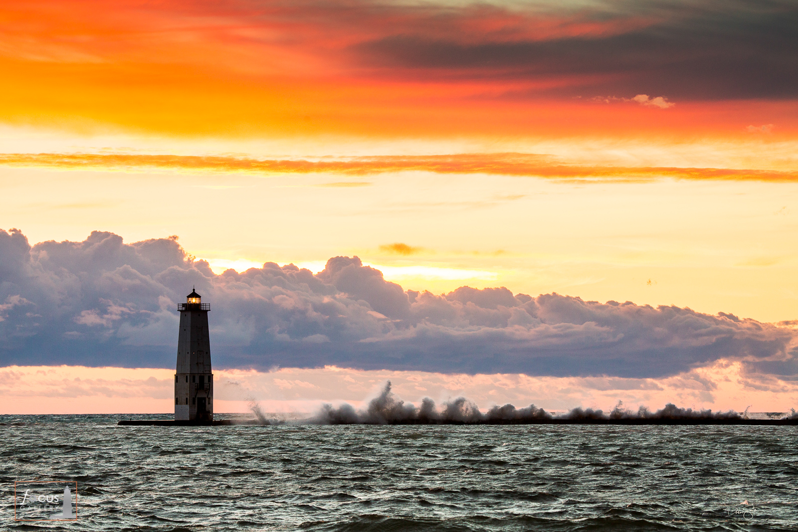 Large waves crash against the Frankfort North Breakwater Lighthouse during a colorful sunset.