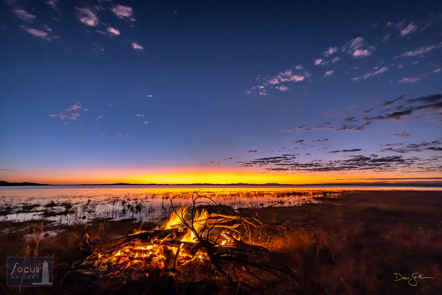 A bonfire burns on the shores of Lake Kariba at sunset as the last light of day glows in the sky.