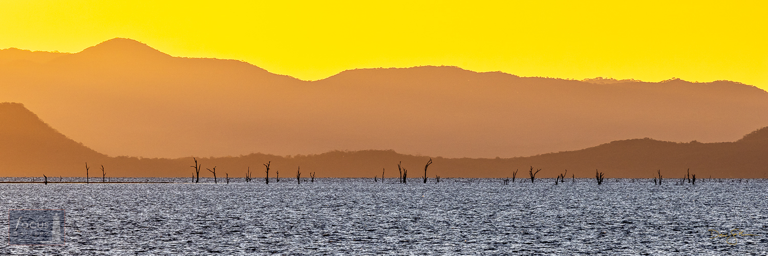 A colorful sunset drapes the mountains, submerged trees and waters of Lake Kariba in beautiful shades of light.